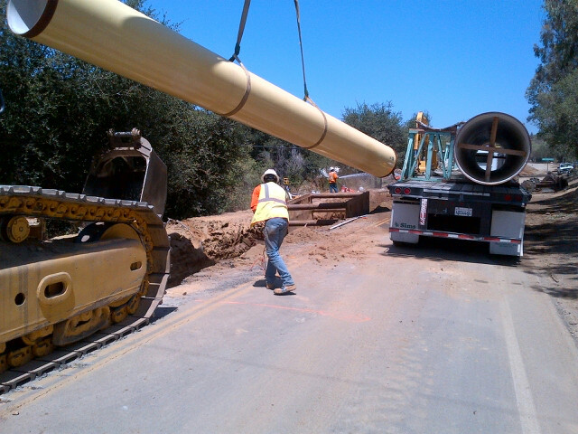 Large infrastructure pipe being positioned by lifting equipment during an active underground pipeline installation