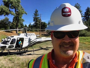 Oskar Granquist wearing a hard hat and safety vest at an infrastructure worksite with a helicopter behind him