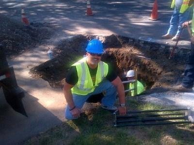 Oskar Granquist wearing a blue hard hat at an underground utility trench during field construction operations